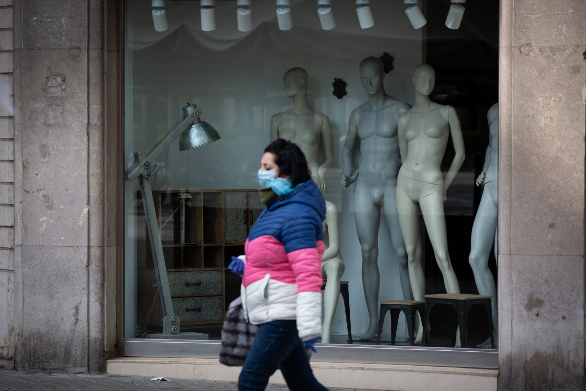 Una mujer protegida con una mascarilla pasa junto a un escaparate de una tienda cerrada durante el noveno día laborable desde que se decretó el estado de alarma en el país a consecuencia del corona
