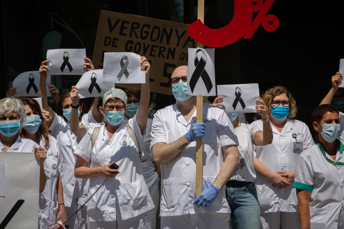 Trabajadores sanitarios protegidos con mascarilla se reúnen a las puertas del Hospital Clínic de Barcelona con pancartas y crespones negros para reivindicar contratos dignos y más personal, así co