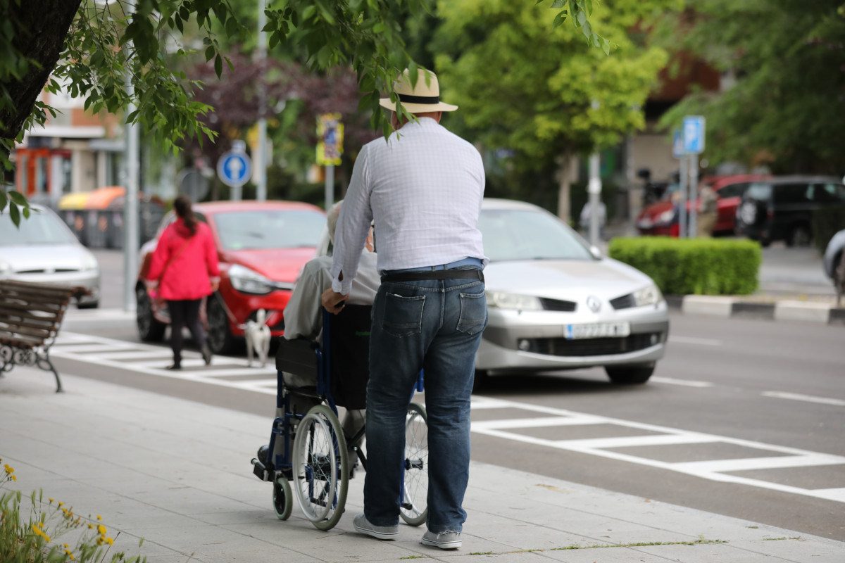 Un hombre pasea a una persona de edad avanzada en silla de ruedas durante su franja horaria permitida en la desescalada por la crisis del Covid-19 donde aquellos mayores de 70 años pueden salir a la 