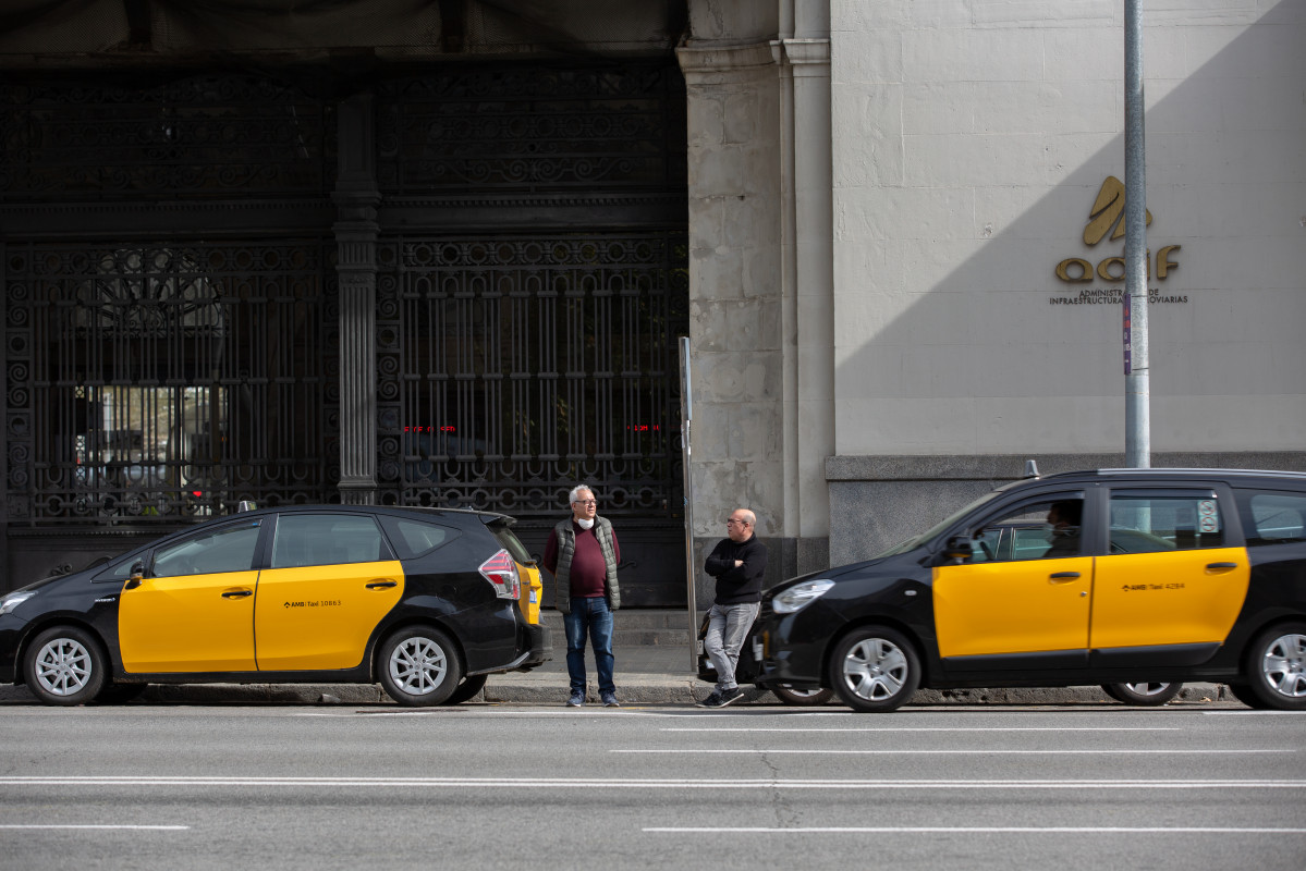 Dos taxistas esperan fuera de sus coches a recoger algún pasajero en una estación de tren de Barcelona durante el tercer día laborable del estado de alarma por coronavirus, en Barcelona/Catalunya (