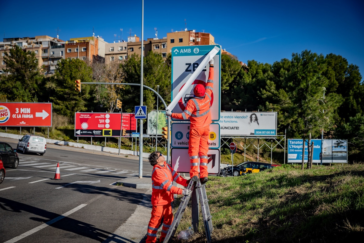 Operarios instalando las señales de tráfico definitivas de la ZBE Rondas BCN en el ramal de la salida 14 Besòs de la Ronda de Dalt, en L'Hospitalet de Llobregat