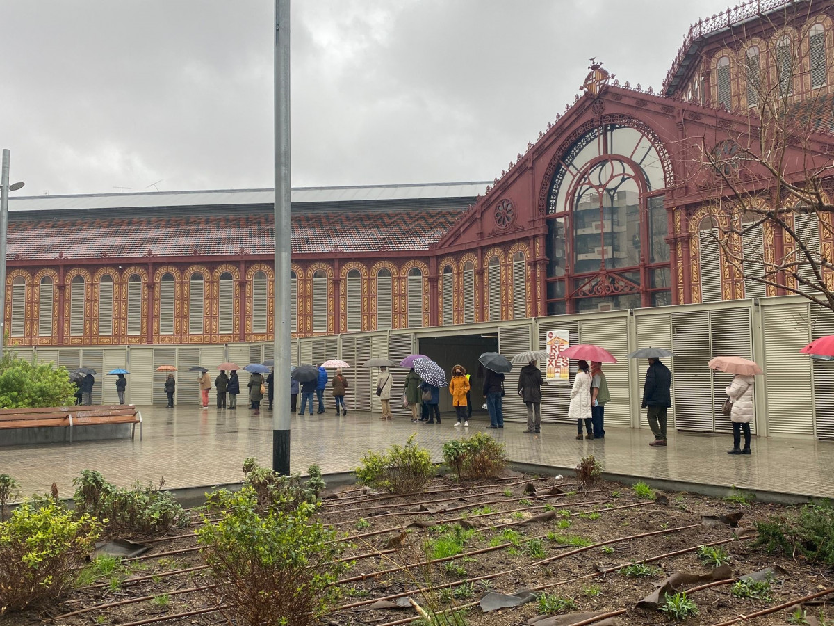 Cola de ciudadanos guardando distancia de seguridad por el coronavirus esperando a votar en el Mercado Sant Antoni de Barcelona en las elecciones catalanas