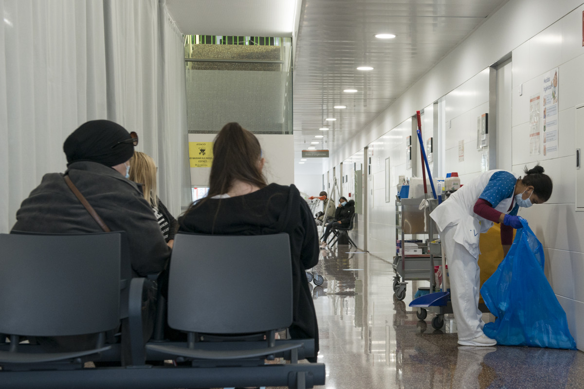 Varias pacientes esperan en una sala de espera mientras una mujer limpia en el CAP Masdevall el día en el que comienza la campaña de vacunación antigripal en la región, en Figueres, Girona (Catalu