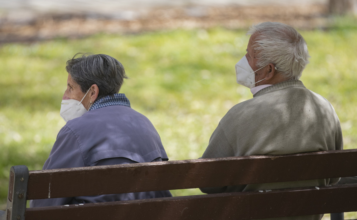 Un hombre y una mujer mayores, sentados en un banco y con mascarilla, en el Parque del Manzanares, el día en que entra en vigor el uso obligatorio de mascarilla incluso con distancia de seguridad, en