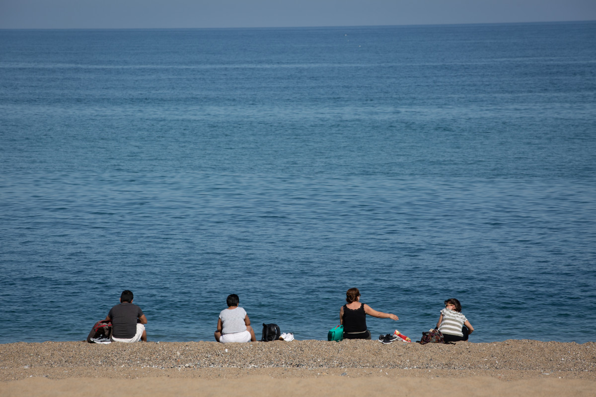 Varias personas sentadas en la Playa de la Barceloneta respetan la distancia de seguridad.