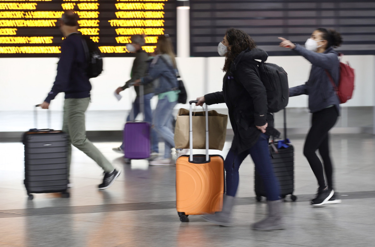 Varias personas, con maletas, pasan junto a un panel de salidas con diferentes destinos, en la estación Madrid - Puerta de Atocha