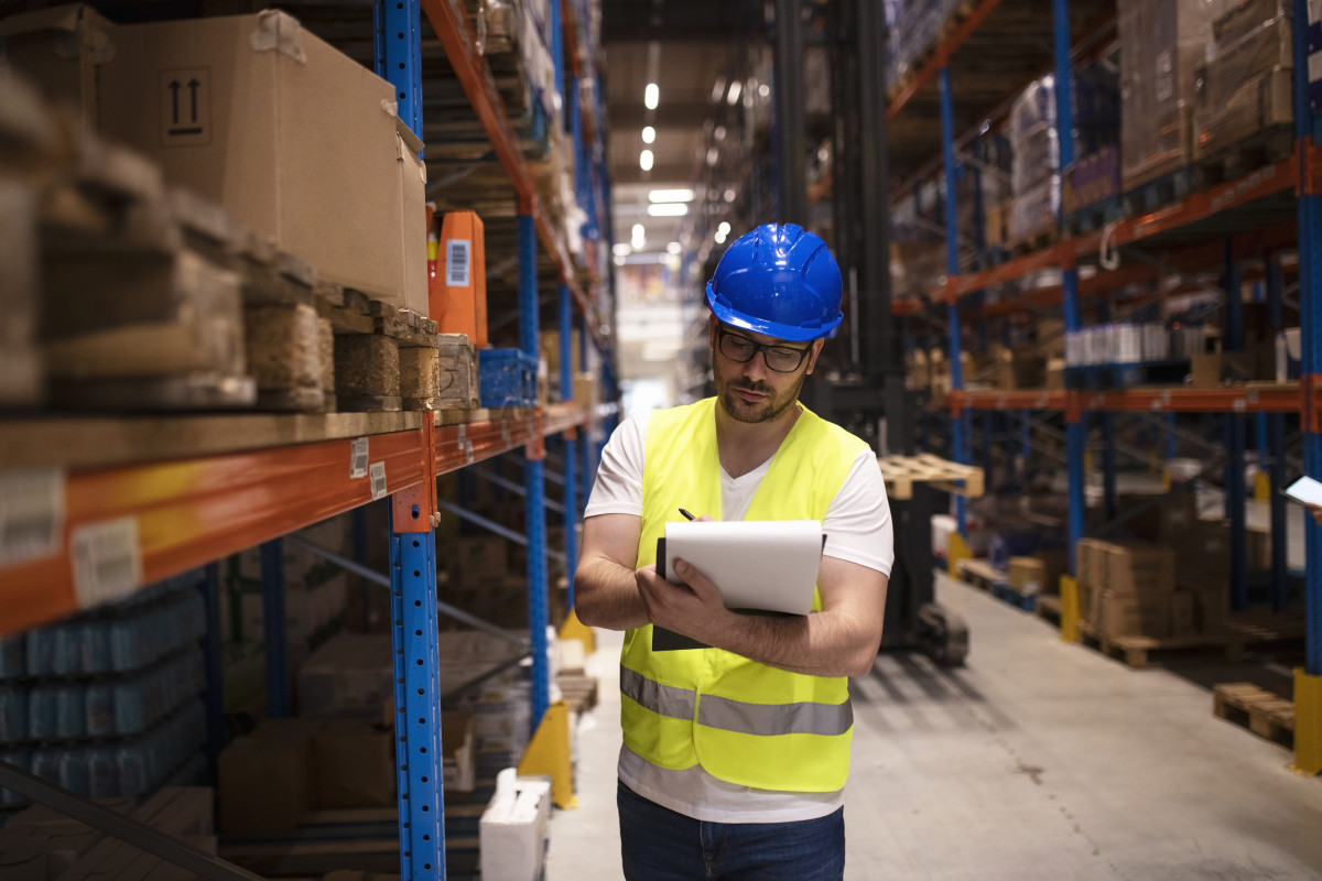 Trabajador de almacen anotando informe de inventario sobre productos en area de almacenamiento grande