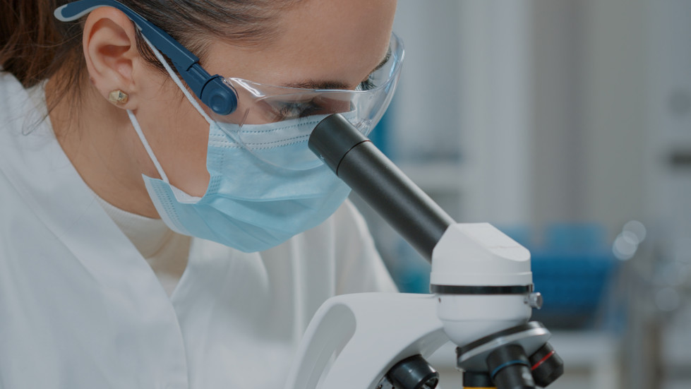 Specialist analyzing dna microscope laboratory wearing face mask glasses gloves protection science engineer using magnifying glass optical microscopic tool close up
