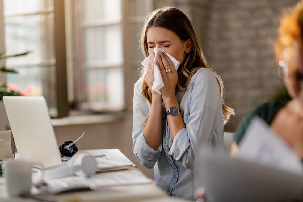 Young sick businesswoman sneezing tissue while working office